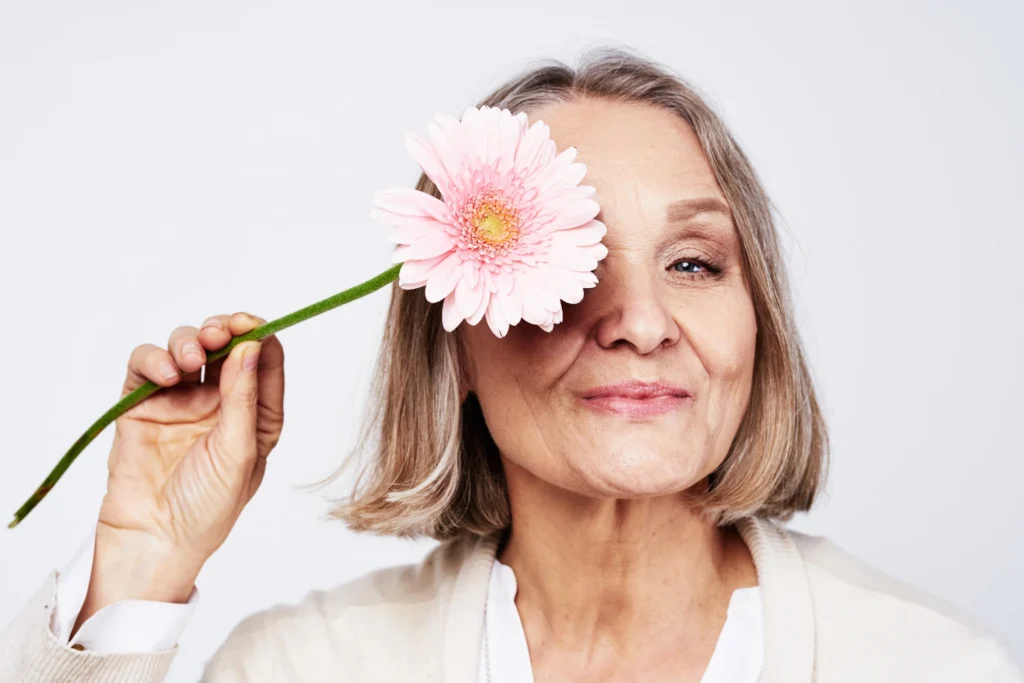 A mature woman is holding a flower and covering her face with it